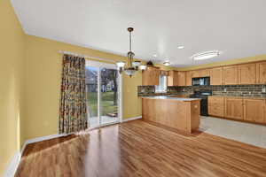 Kitchen featuring a peninsula, a chandelier, black appliances, tasteful backsplash, and hanging light fixtures
