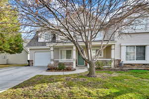 View of front of property with stone siding, a front yard, a porch, concrete driveway, and a shingled roof