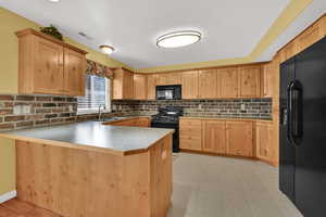 Kitchen with black appliances, a peninsula, tasteful backsplash, light brown cabinetry, and light countertops