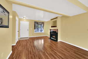 Unfurnished living room featuring a lit fireplace, wood finished floors, and beam ceiling