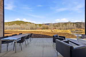 Spacious concrete patio featuring an expansive mountain backdrop, an adjacent body of water, and surrounding natural foliage