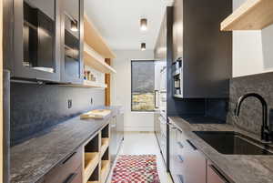 Kitchen featuring glass fronted cabinets, open shelves, dark stone counters, stainless steel appliances, and modern cabinets