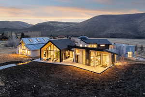 Back of property at dusk featuring a patio, a standing seam roof, a mountain view, and stone siding