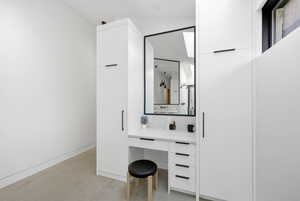 Integrated vanity desk with a rectangular mirror, white cabinetry, and matte black hardware