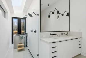 Modern bath with a freestanding cylindrical tub, walk-in shower featuring a rain showerhead, a dual vanity with undermount sinks, and a large wall-mounted mirror
