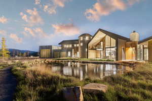 Contemporary architectural residence featuring a prominent A-frame section, stone and wood-paneled exterior, a unique cylindrical stone tower, and expansive glazing overlooking a reflective pond
