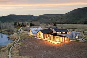 Expansive property featuring multiple structures with modern architectural elements, a prominent pond, and surrounding mountain terrain
