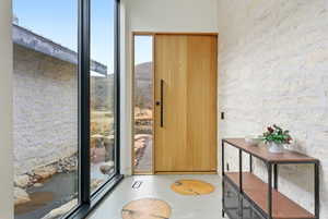 Modern entry featuring a full-light wood-paneled door with vertical hardware, floor-to-ceiling windows, and a stone accent wall