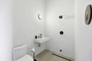 Modern utility space featuring a wall-mounted sink with matte black faucet, a sleek toilet, and a shower with dark fixtures