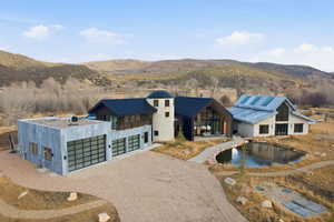 Expansive property featuring three distinct structures with a gravel driveway, a private pond, and mountain scenery