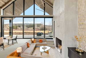 Living area featuring a high ceiling, a warm lit fireplace, floor to ceiling windows, plenty of natural light, and a mountain view