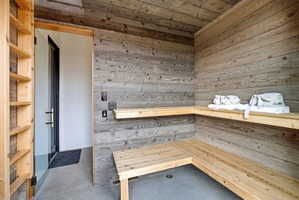 Wood-paneled room featuring built-in wooden benches and shelving, concrete flooring, and a glass-paneled door with dark hardware