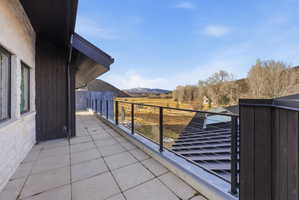 Expansive outdoor terrace featuring light-toned square pavers, a black metal and glass railing, and a contrasting dark wood-paneled exterior wall