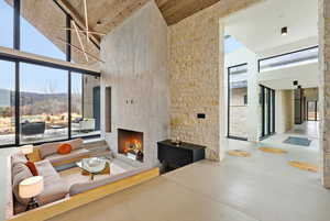 Living area with a high ceiling, a lit fireplace, finished concrete flooring, and expansive windows