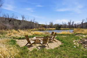 Outdoor fire pit area with gravel groundcover, four Adirondack chairs, and a natural pond