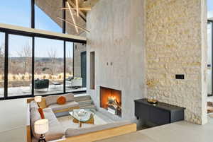 Living area featuring a contemporary fireplace, full-height glass window wall, natural stone accent wall, and a high vaulted ceiling with modern lighting fixtures