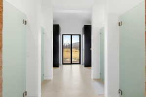 Hallway featuring frosted glass doors, light-toned flooring, white walls, and a black-framed glass door opening to an outdoor landscape