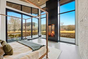 Floor-to-ceiling windows with black framing, a built-in fireplace with a dark metal surround, and light-toned flooring