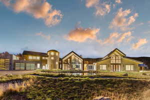 Modern architectural design featuring a prominent silo structure, expansive glass windows, multiple garage bays, stone and paneling facade, and a reflective pond feature