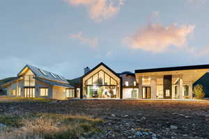 Contemporary architectural design featuring expansive window walls, a striking A-frame structure, a flat roof section, stone veneer siding, and a metal roof
