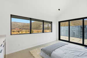 Bedroom with a mountain view, vaulted ceiling, access to exterior, and finished concrete floors