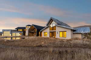 Back of house at dusk featuring a standing seam roof, a balcony, and stone siding