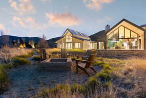 Outdoor fire pit area with stone surround, two modern Adirondack chairs, and a gravel base