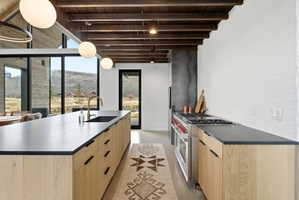Gourmet kitchen featuring a substantial island with integrated sink, natural wood-finish cabinetry, exposed wood beam ceiling, and a professional-grade range