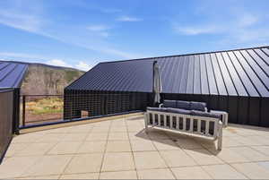 Expansive outdoor patio featuring light-toned square pavers, a black wire railing, and a modern exterior with a standing seam metal roof