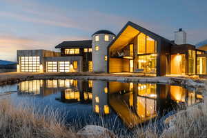 Back of house at dusk with a balcony, a chimney, a standing seam roof, a patio area, and a water view