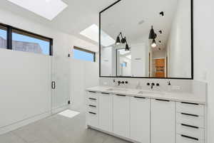 Full bathroom featuring a stall shower, double vanity, a skylight, vaulted ceiling, and concrete floors