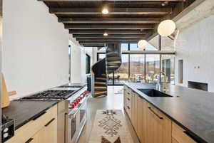 Gourmet kitchen featuring a large range with multiple burners, a spacious island with an integrated sink and brass-finish faucet, dark countertops, and light wood-finish cabinetry