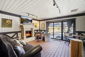 Living area featuring a stone-clad fireplace, sliding glass doors, white paneled walls with dark trim, and a patterned carpet