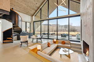 Sunken living room with a mountain view, a high ceiling, expansive windows, a warm lit fireplace, and concrete flooring
