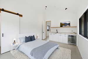 Bedroom featuring a barn door, wine cooler, concrete flooring, bar with sink, and vaulted ceiling