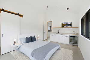Vaulted ceiling room featuring a modern barn door, built-in wet bar with sink, under-counter beverage refrigerator, and black framed windows