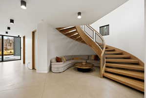 Curved wood staircase with glass and metal railing, concrete flooring, recessed ceiling lighting, and expansive glass doors opening to outdoor elements