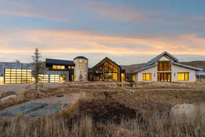 Modern architectural residence featuring multiple structures, a circular stone tower, expansive glass garage doors, a large A-frame window facade, and a reflective pond feature