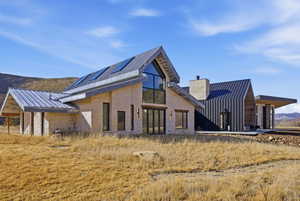 Contemporary residence featuring a stone and vertical metal siding exterior, multiple pitched metal roofs, a prominent stone chimney, and large multi-pane windows