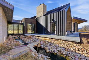 Contemporary exterior showcasing a metal standing-seam roof, stone chimney, and a concrete patio