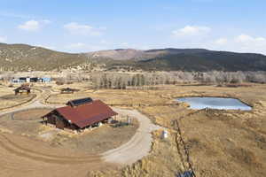 Extensive rural property featuring a barn with a red metal roof and solar panels, a circular driveway, a fenced riding arena, and a pond surrounded by natural landscaping