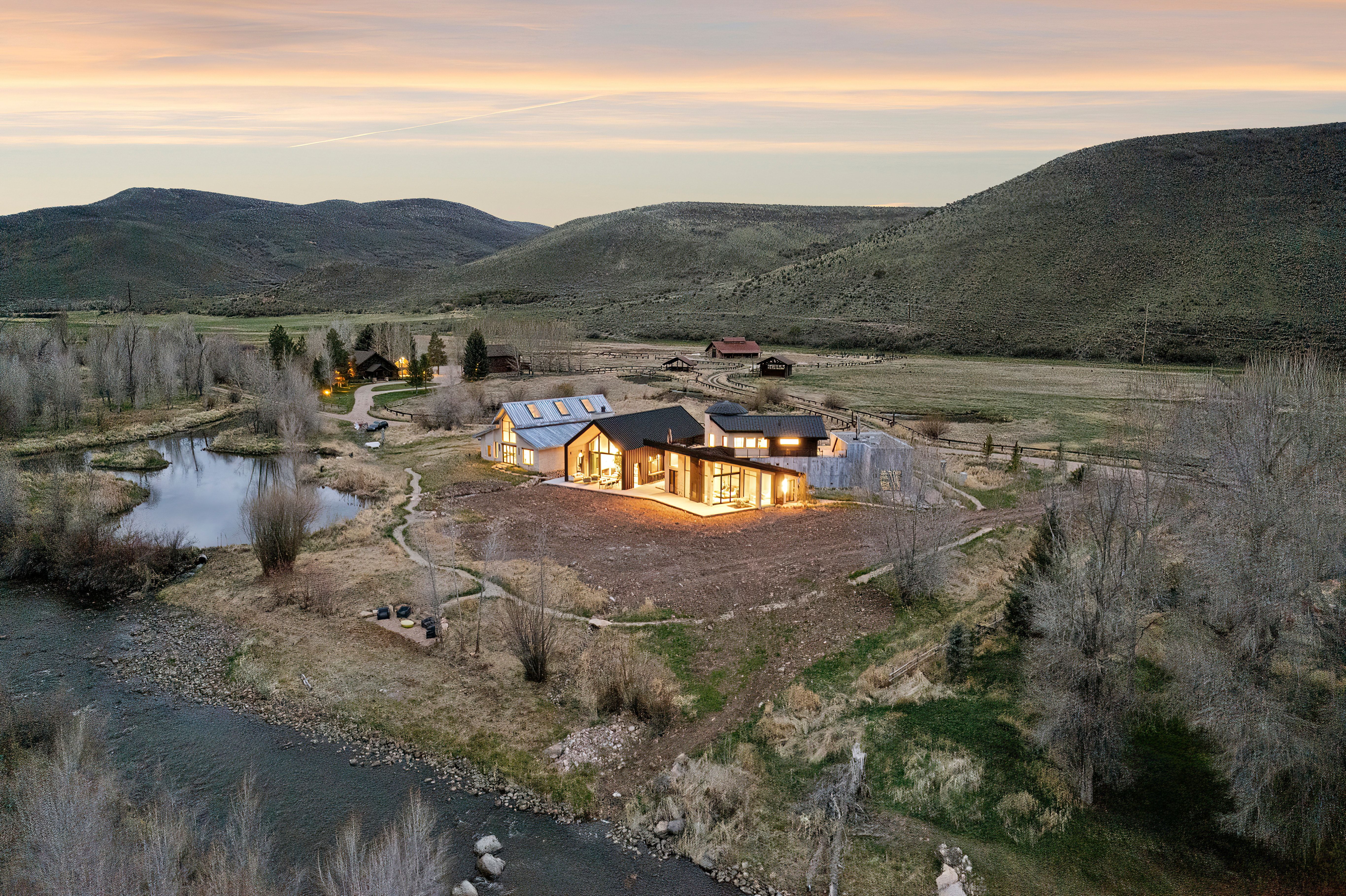 Modern architectural residence with expansive glass facades, a detached barn-style structure, and a large private pond