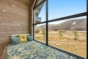 Expansive floor-to-ceiling windows featuring black framing, a built-in window bench, natural wood plank wall finishes, and a mountainous landscape backdrop
