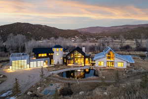 Back of house at dusk with driveway, a mountain view, a swimming pool, and a chimney