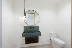 Modern powder room featuring a wall-mounted basin sink with matte black fixtures, a contemporary round mirror, and a sleek toilet