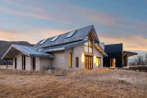 Property exterior at dusk with a standing seam roof, stone siding, a patio area, and roof mounted solar panels