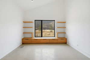 Room with a large black-framed window, built-in wood cabinetry, floating wood shelving, vaulted ceiling, and light-toned flooring