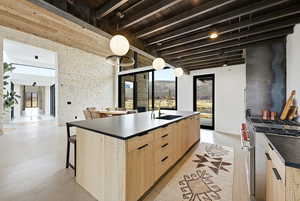 Kitchen featuring light wood finish cabinetry, modern cabinets, high end stainless steel range oven, an island with sink, and decorative light fixtures