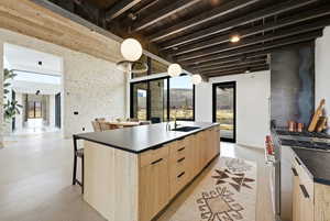 Kitchen featuring a large wood-finish island with a dark countertop and integrated sink, a range with a dark metal hood, exposed wood beam ceilings, and large glass doors
