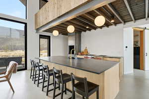 Kitchen featuring a kitchen bar, concrete floors, a large island, light wood finish cabinetry, and dark countertops